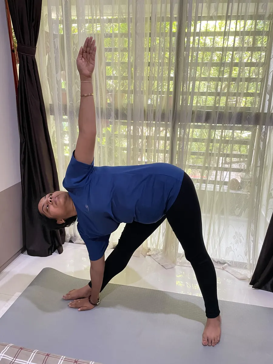 Student extending into triangle pose beside a bright window