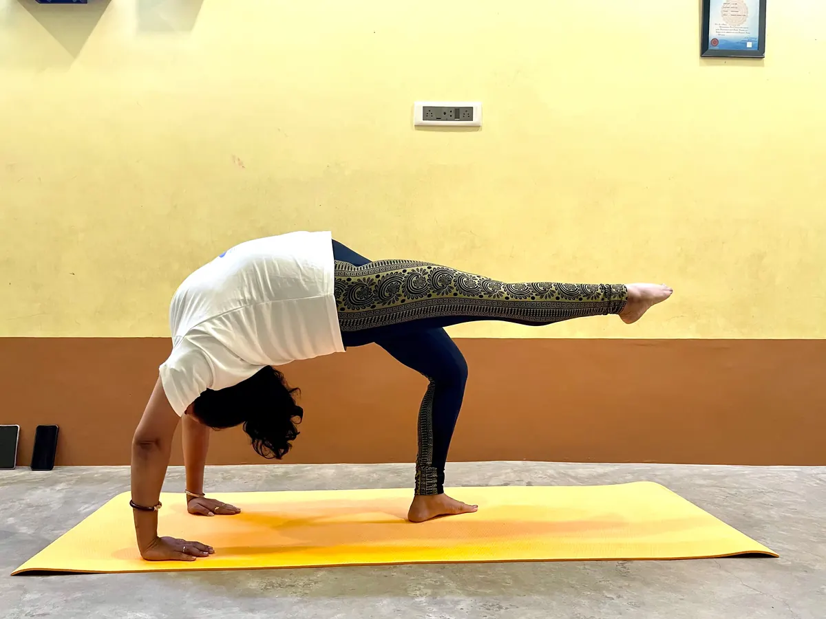 Student lifting one leg skyward in a one-legged wheel backbend at the centre