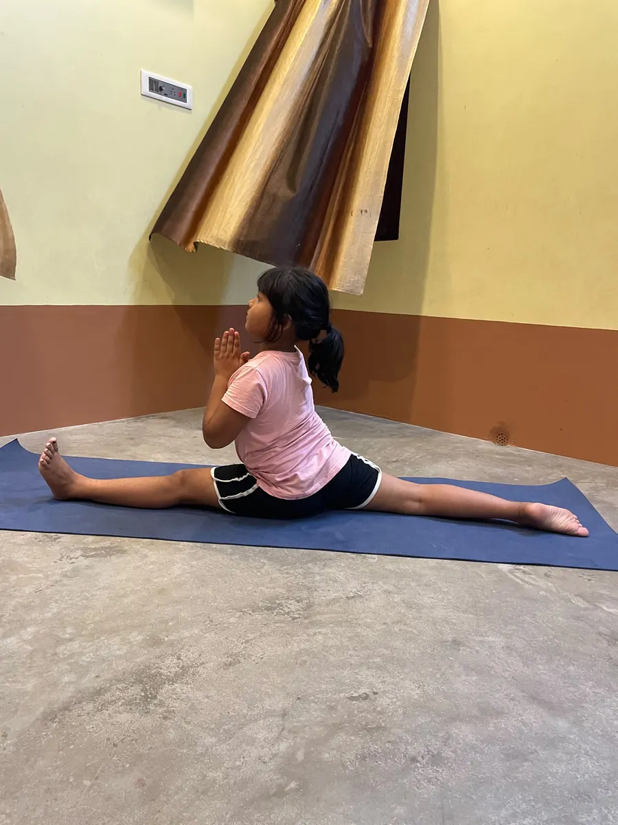 Young student in a full front split with hands folded in prayer